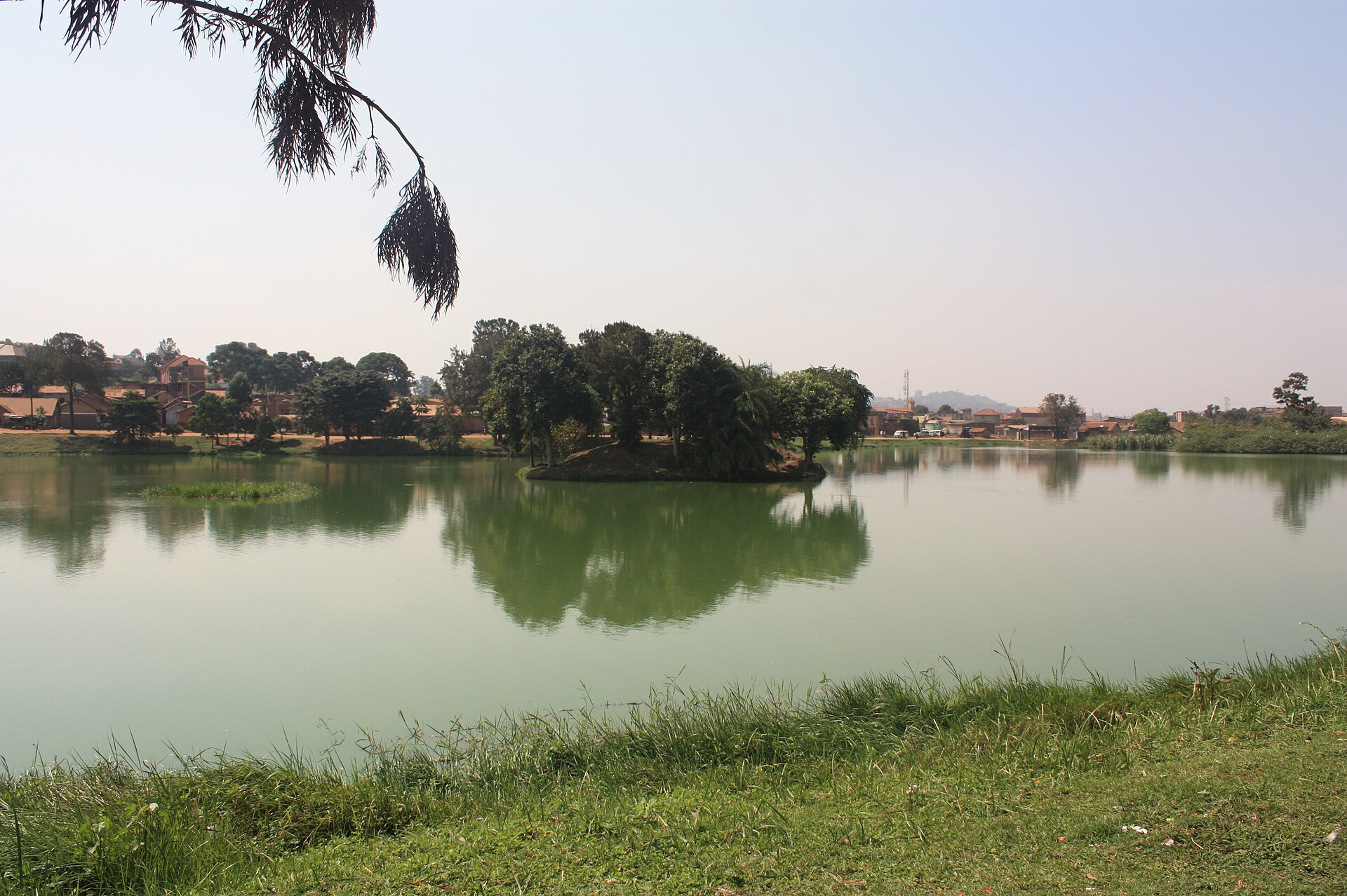 Kabaka's Lake in Ndeeba, showing calm water, a small wooded island and grassy shoreline.